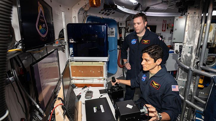 Two astronauts look at a computer screen within a simulated space station.