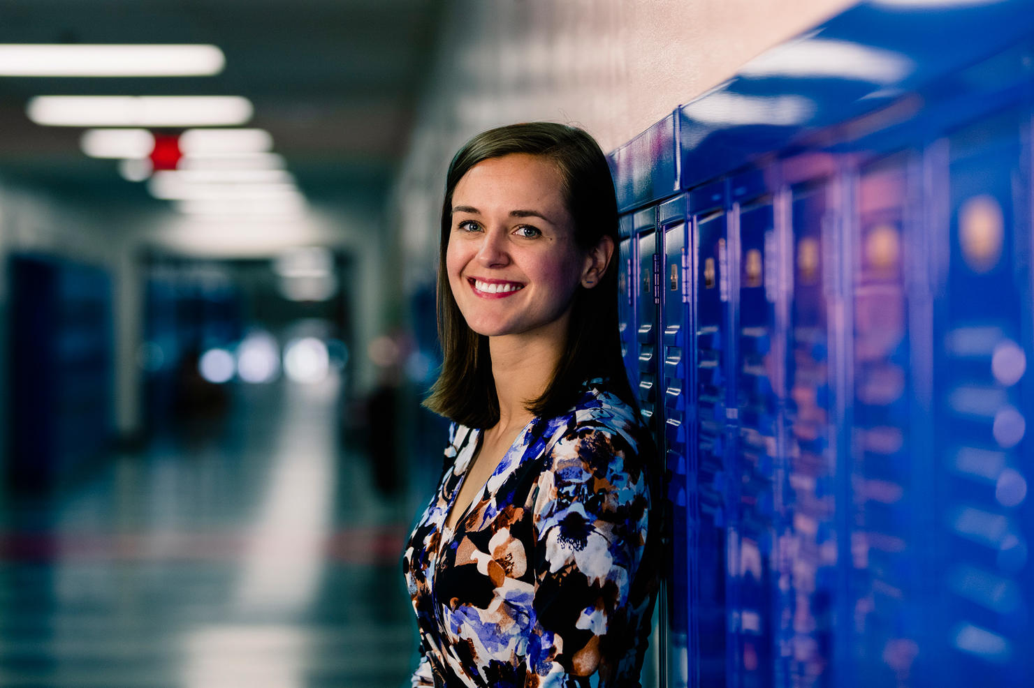 Headshot of Sarah Parshall. She is standing by the lockers in a school hallway.