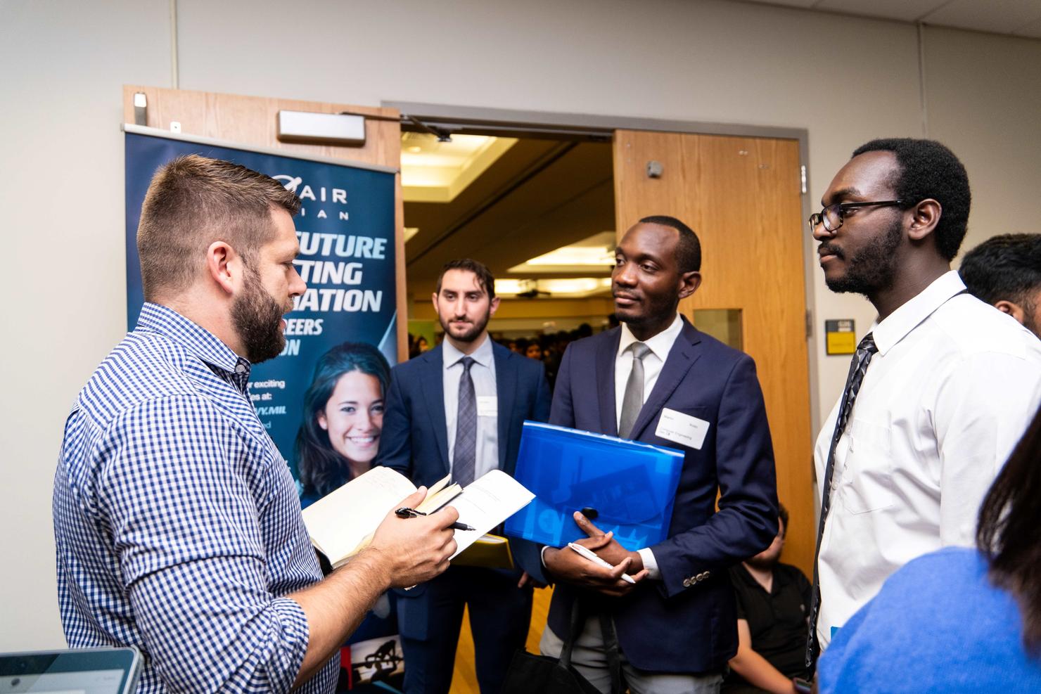 A group of male students speak to a recruiter at the Fall Career Fair