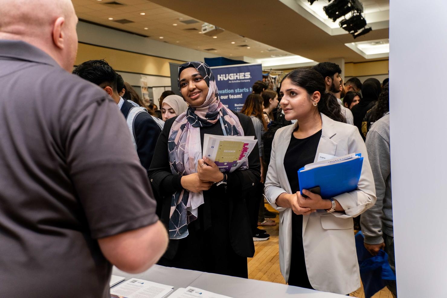 Two female Mason students speak with an employer at the Career Fair