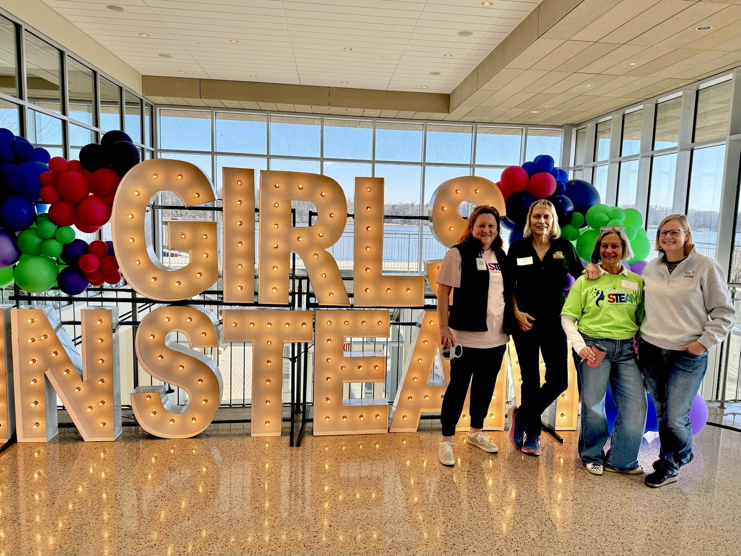 Event organizers in front of the decorative sign that says GIRLS IN STEAM