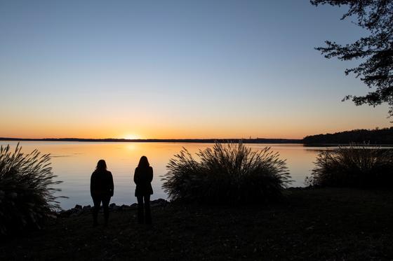 Two people stand in sillouette at the water's edge at sunset at Point of View retreat center